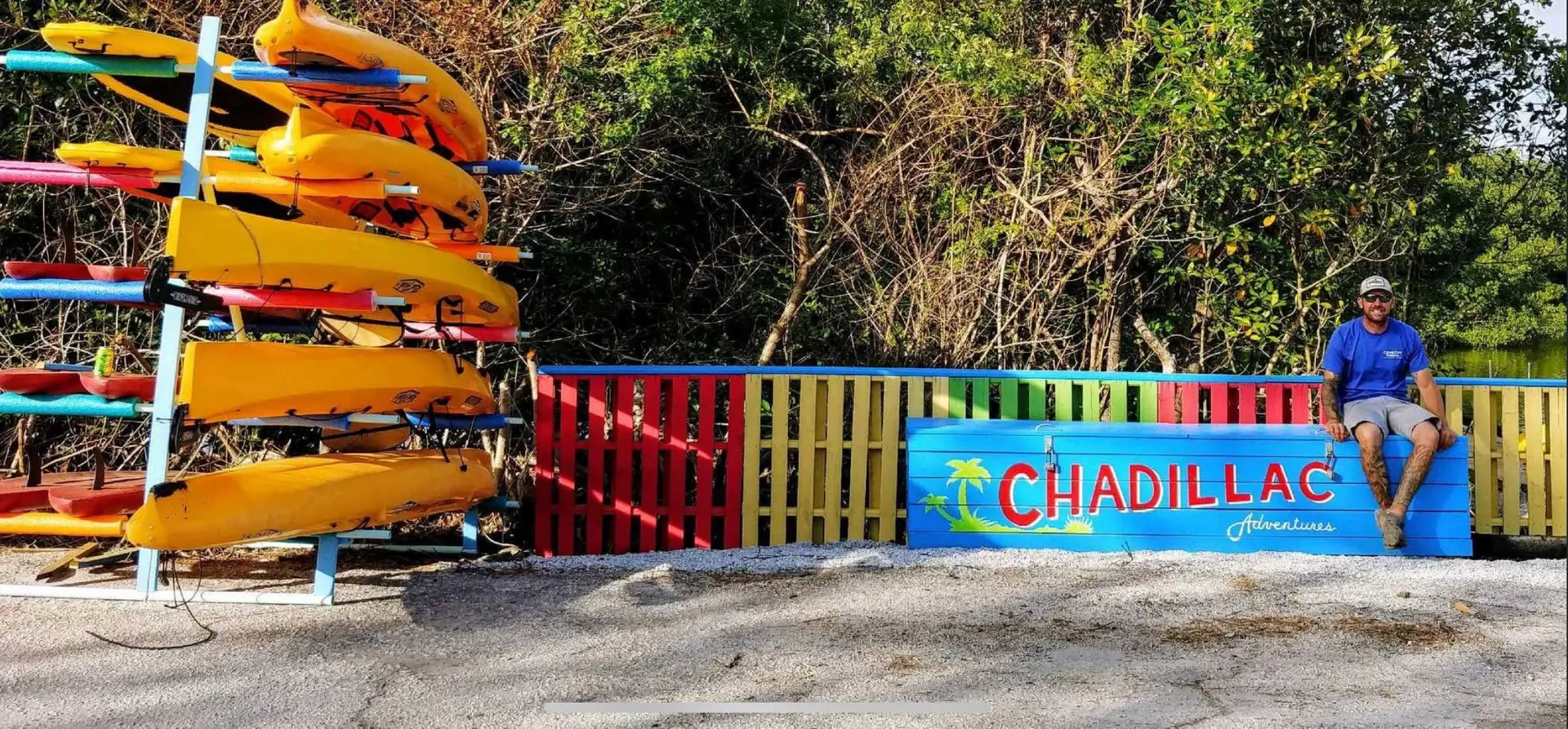 Chad sitting on sign next to Kayaks